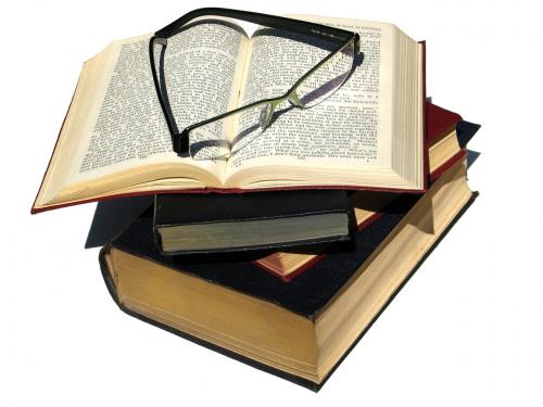 Stack of four books, with the top one open, with reading glasses on top